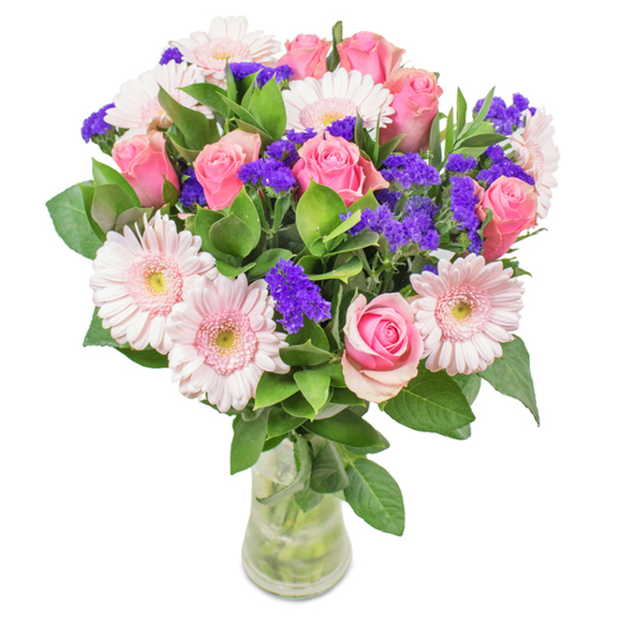 Displayed with elegant clarity against a bright backdrop, this vibrant bouquet features a refined blend of about 7-9 pink roses-some with their petals gently curled, others just beginning their signature spiral, evoking the celebrated blooms of Leytonstone's spring fairs. These are beautifully accompanied by approximately 5-7 pale pink gerbera daisies, their large circular heads and nearly white centres reminiscent of the playful, petal-strewn paths through Cann Hall Park. Interspersed are vivid purple statice or limonium, adding both texture and intensity, their rich colour echoing the creative murals along Leytonstone High Road. An abundant wealth of deep green foliage forms a lush base, echoing the freshness of the area's urban greenery. The clear glass vase allows the fresh stems and water to shine, giving the arrangement a sense of immediacy and natural beauty-perfect for celebrating birthdays, anniversaries, or marking a special moment at home or in the office. This bouquet, a harmonious blend of pink roses, gerberas, and purple accents, captures both the romance and cheerful energy of Leytonstone, offering a heartfelt token from your local florist.